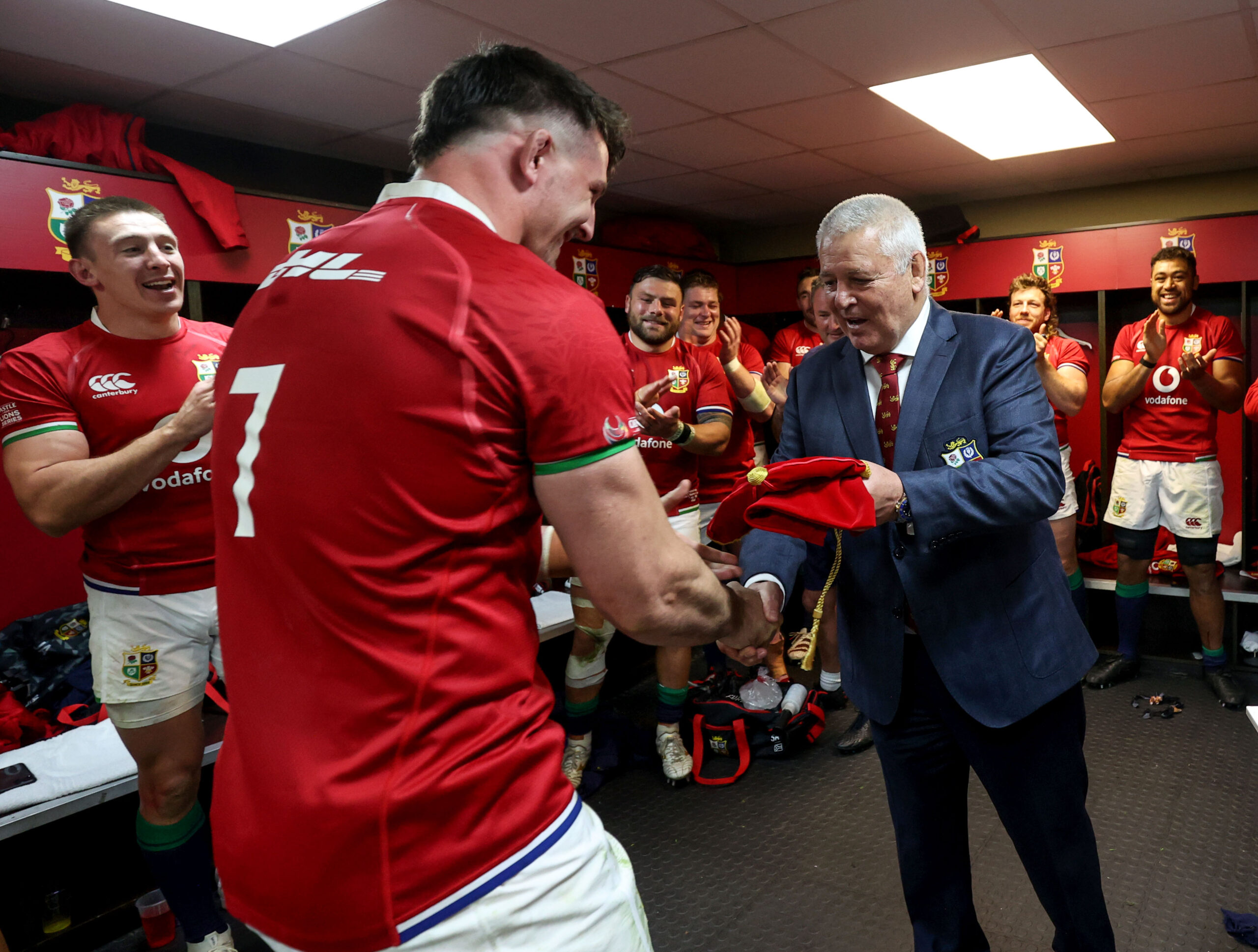 Warren Gatland presenting Tom Curry's Lions Honour Cap, with Josh Adams, Tadhg Furlong, Taulupe Faletau and others applauding.