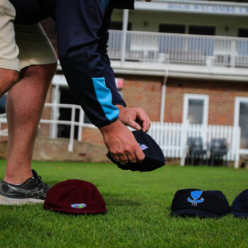 Chris Sketchley setting down four baggy cricket caps on the ground: West Indies, Yorkshire, Sussex and Essex baggy caps.