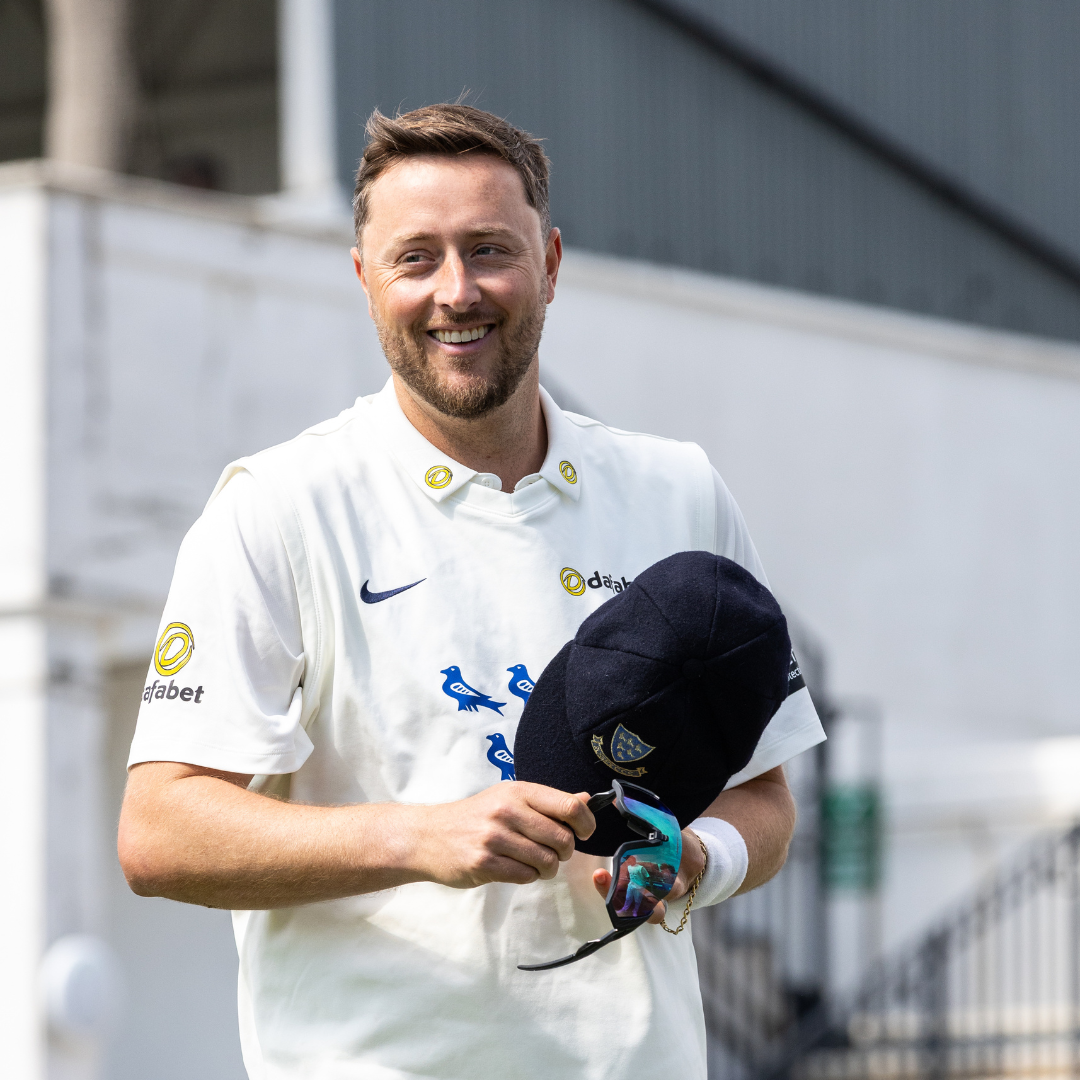 Ollie Robinson holding his Sussex baggy cap and looking cheerfully at the camera.